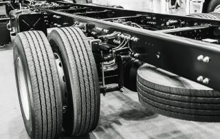 black and white close up of a truck trailers back wheels and suspension. Image depicts the overall anatomy of a heavy truck suspension system