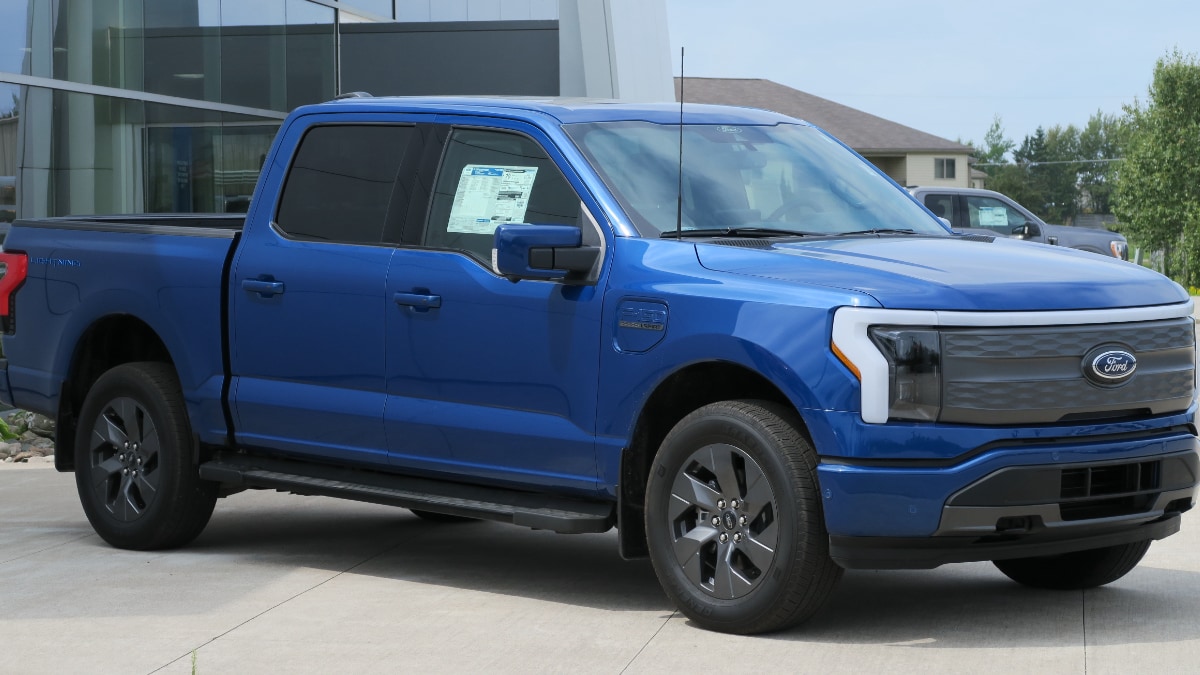 A blue pickup truck in a parking lot in need of repairs. Attribution to Elise240SX.